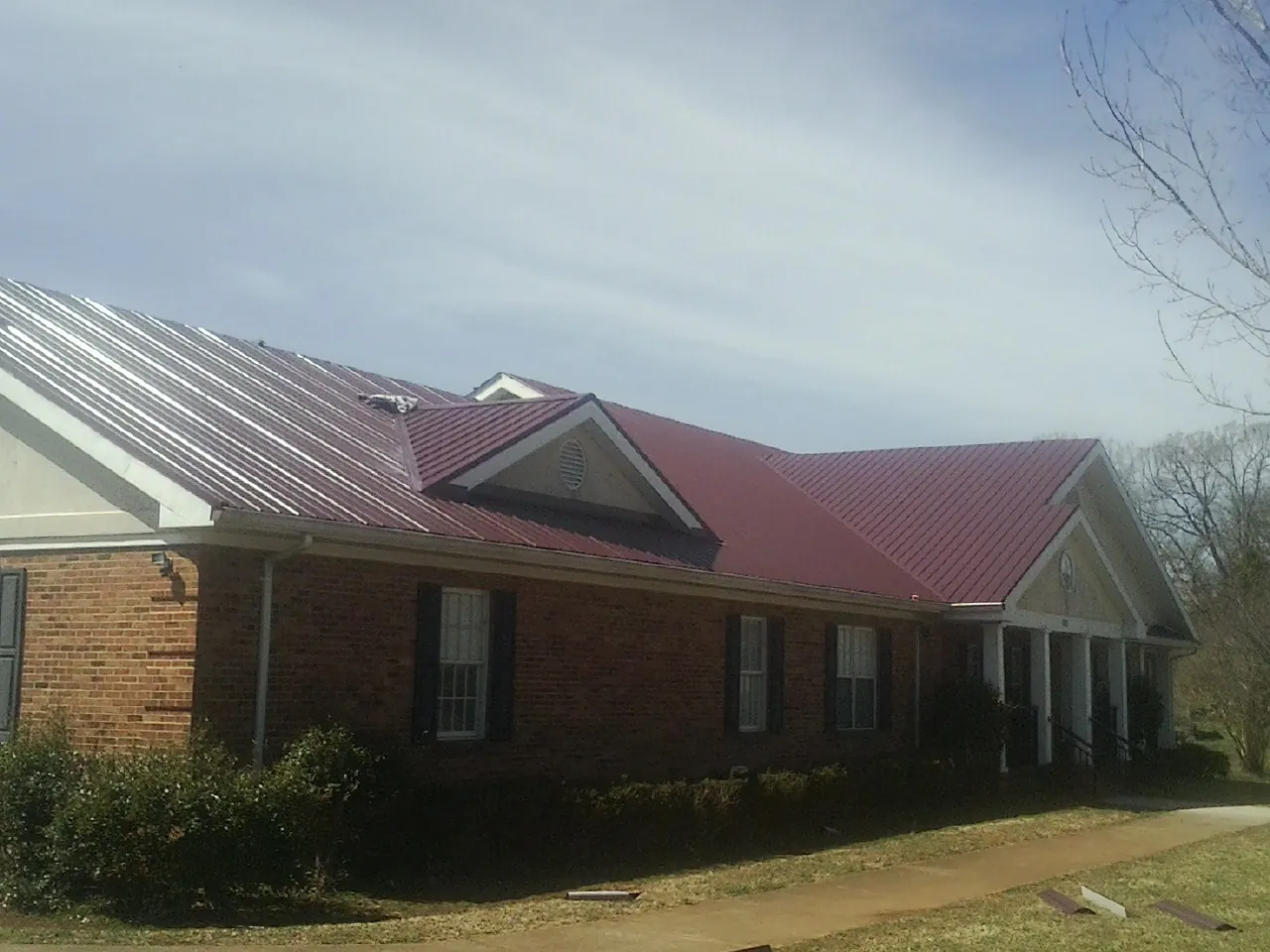 Red metal roof with gabled entries on a long brick building, from a Hail Damage Roof Repair job in Enterprise