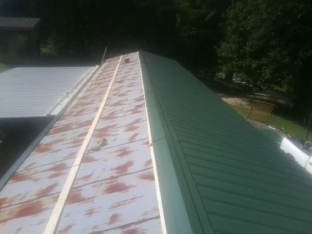 Old rusted panels beside newly installed green metal roofing — Wind Damage Roof Repair by Roofing Brothers in Enterprise