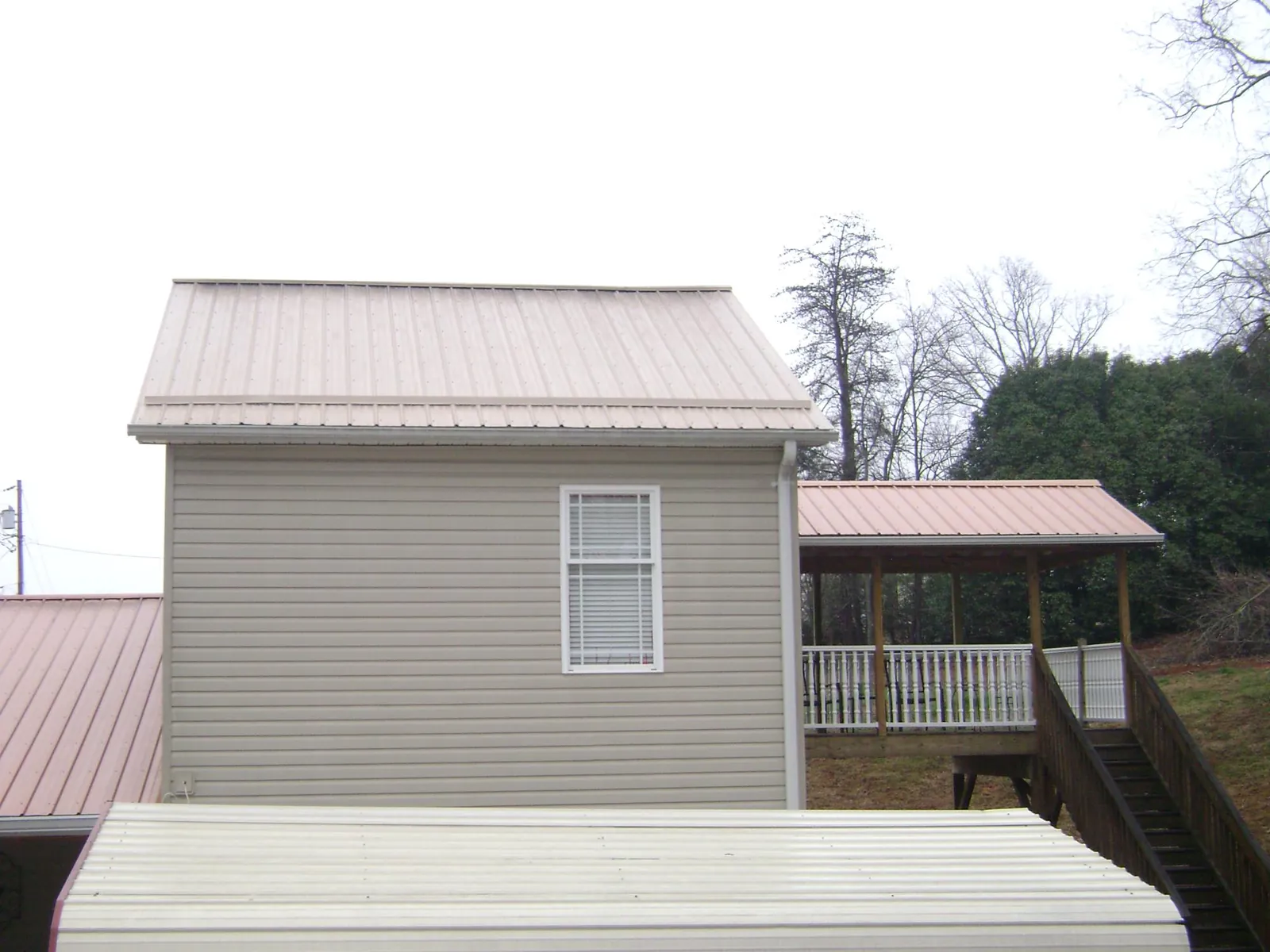 Tan metal roofs on a two story addition and attached porch, from a Roof Replacement job in Enterprise